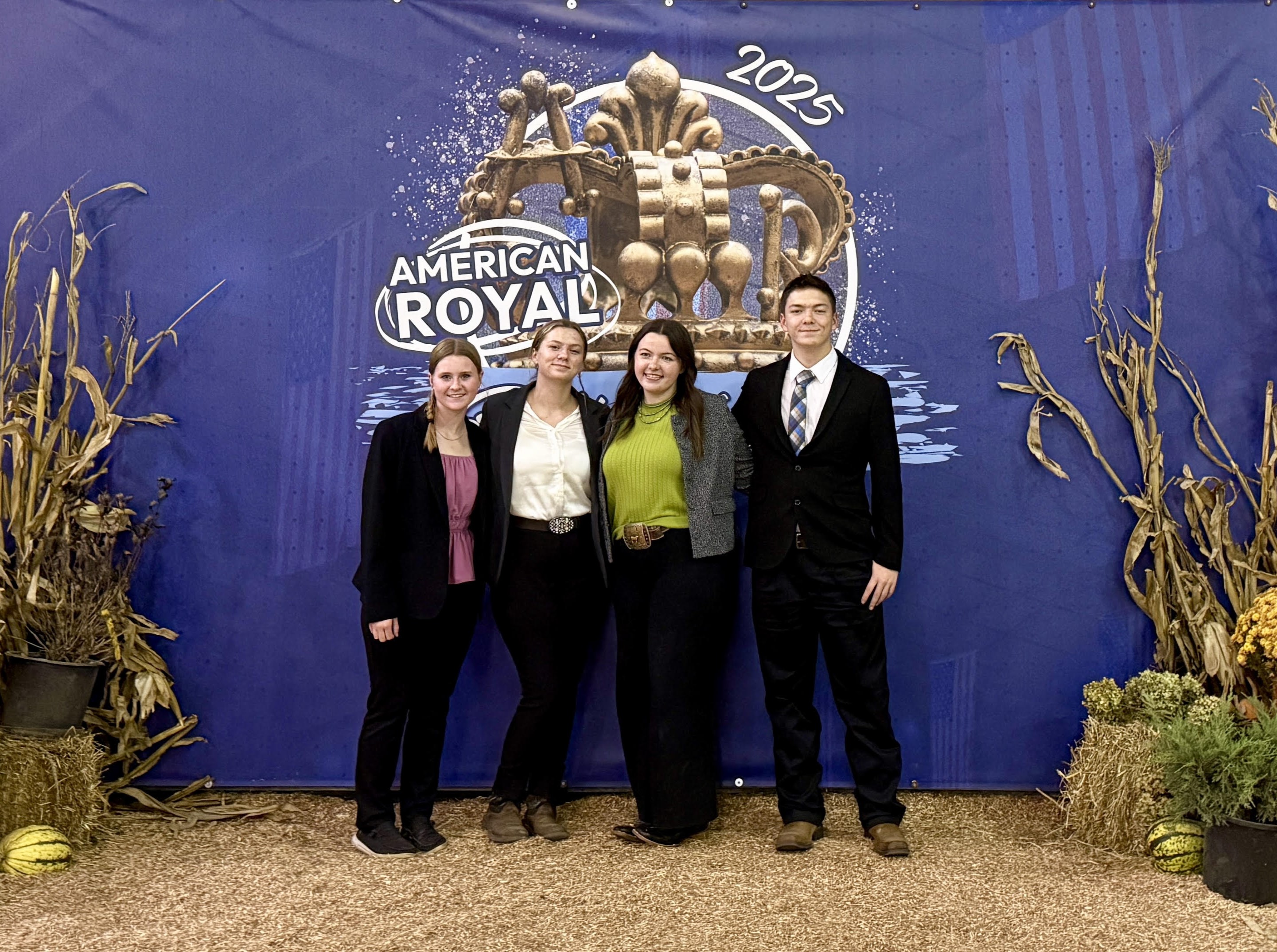 Four youth with their arms around each other standing in front of the 2025 American Royal sign.